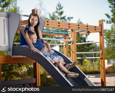 Mother and six year old boy child sitting together on the slide