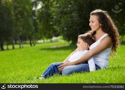 Mother and small son sit on a summer garden lawn