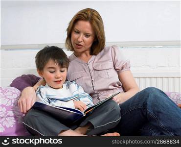 Mother and son (5-6) reading book on couch in living room