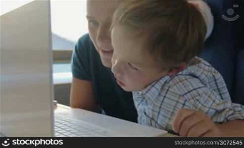 Mother and son are watching something in laptop and discussing it lively, son is hugging mom.