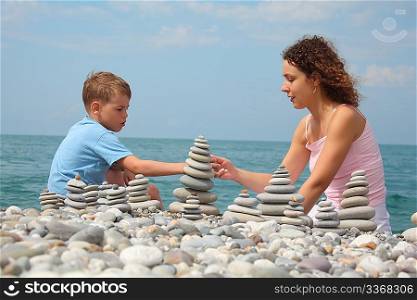 mother and son builds stone stacks on pebble beach