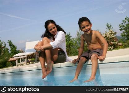 Mother and son dipping feet in swimming pool