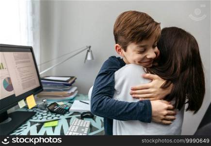 Mother and son hugging while she telecommutes from home. Mother and son hugging while she telecommutes