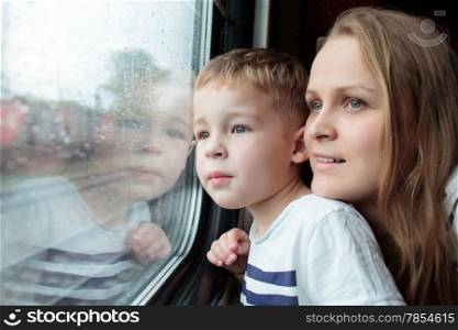 Mother and son looking through a train window as they enjoy a days travel with the small boys face reflected in the glass