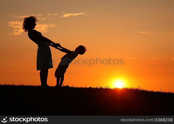 Mother and son on sunset holding by hands