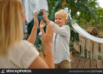 Mother and son play on terrace at the trailer, summer camping. Family with kids travel in camp car, nature and forest on background. Campsite adventure, travelling lifestyle, campers. Mother and son play on terrace at the trailer