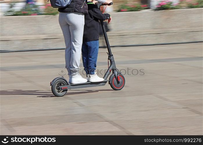 Mother and son riding electric kick scooter at the city square, blurred motion