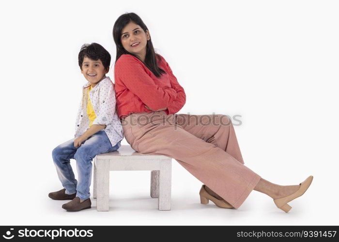 Mother and son sitting together on a wooden stool against white background