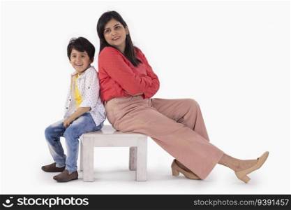 Mother and son sitting together on a wooden stool against white background