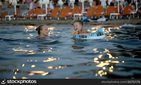Mother and son swimming in the sea in the evening. They laughing and fooling, boy using rubber ring. Family summer vacation