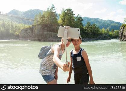 Mother and son taking selfie on mobile phone with stick. Vacation on river in the mountain. selfie on mobile phone with stick