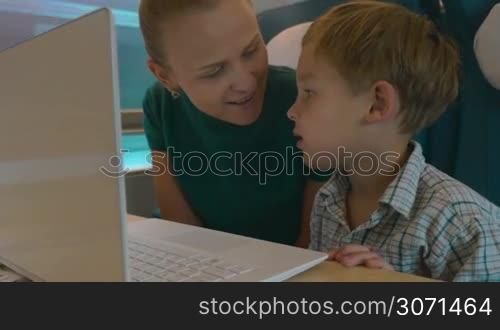Mother and son using laptop for entertainment speaks during the travel by train