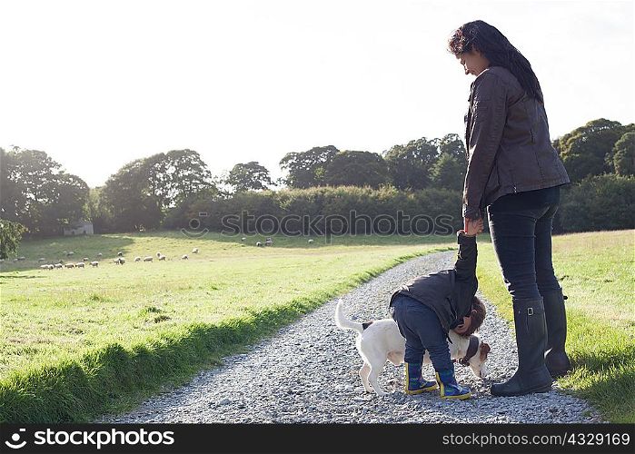 Mother and son walking dog on dirt road