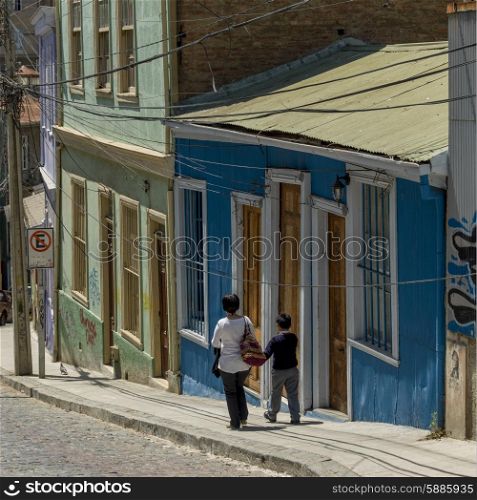 Mother and son walking on street along houses, Valparaiso, Chile