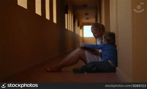 Mother and son with a book sitting on the floor of hotel hall. Mom teaching her lilttle child