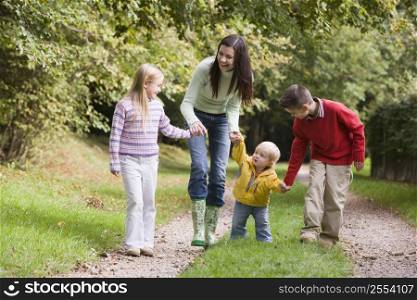 Mother and three young children walking on path outdoors smiling