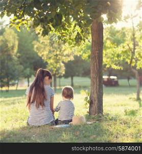 Mother and toddler sitting under the tree during summer leisure