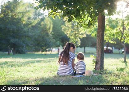 Mother and toddler sitting under the tree during summer vacation