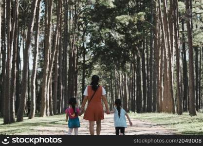 Mother and two daughters holding hands and take a walk in the pine forest on a spring day.