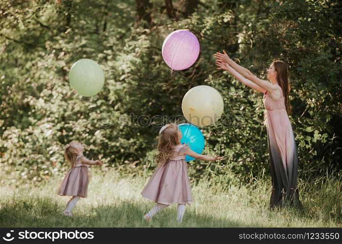 Mother and two daughters holding hands circling. Family time together. Girls with balloons. Soft focus. Funny time. Mother and two daughters holding hands circling. Family time together. Funny time. Girls with balloons. Soft focus