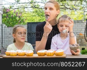 Mother and two daughters lick spoons with confectionery icing for Easter cupcakes