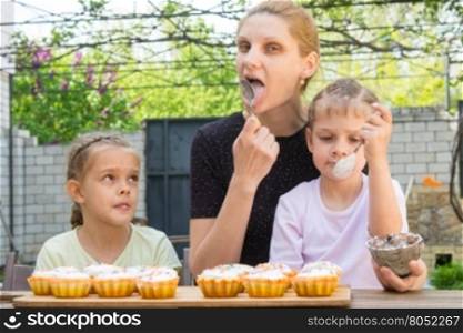 Mother and two daughters lick spoons with confectionery icing for Easter cupcakes