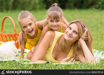 Mother and two daughters lie on each other on the green grass