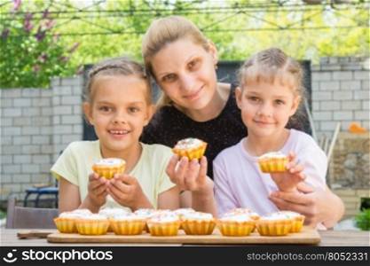 Mother and two daughters sitting at the table with Easter cupcakes in his hands and looked into the frame