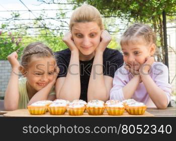 Mother and two daughters with a good appetite and big eyes looking at easter cupcakes