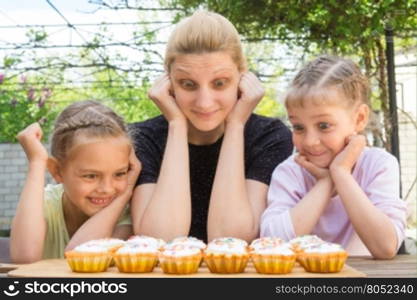 Mother and two daughters with a good appetite and big eyes looking at easter cupcakes