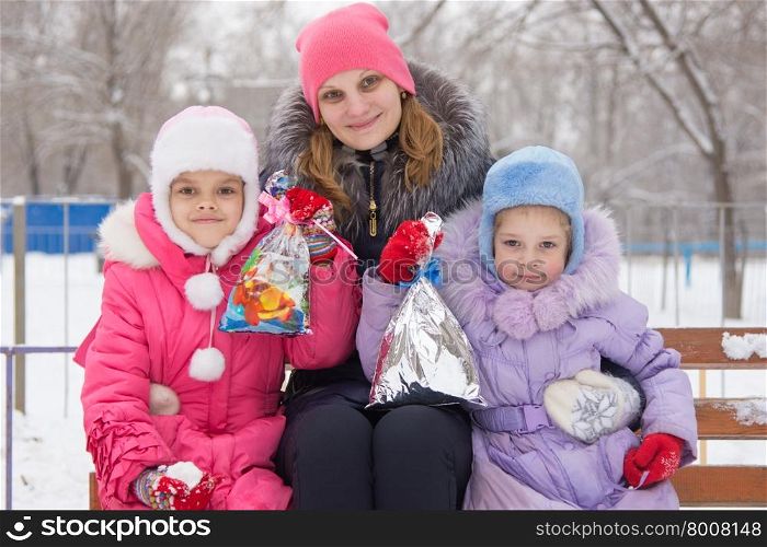 Mother and two daughters with Christmas gifts in his hands. Happy mother and two daughters with Christmas gifts in hands on a snowy street in winter weather