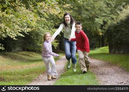 Mother and two young children running on path outdoors (selective focus)