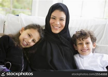 Mother and two young children sitting in living room smiling (high key/selective focus)