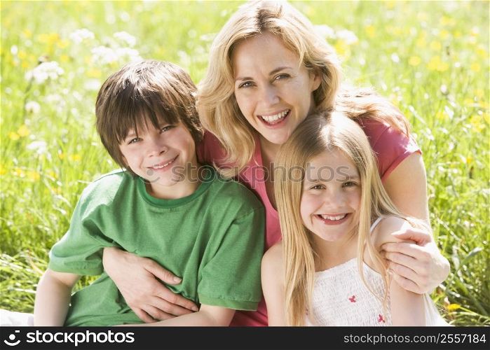 Mother and two young children sitting outdoors smiling