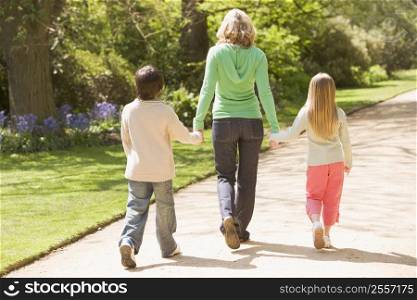Mother and two young children walking on path holding hands smiling