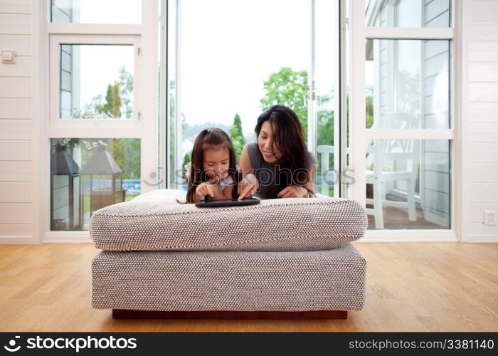 Mother and young daughter using a digital tablet in a living room interior