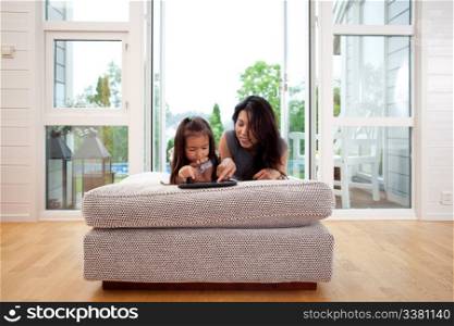 Mother and young daughter using a digital tablet in a living room interior