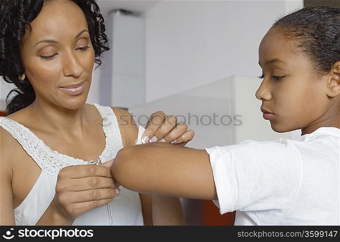 Mother applying bandaid to daughter (7-9) indoors