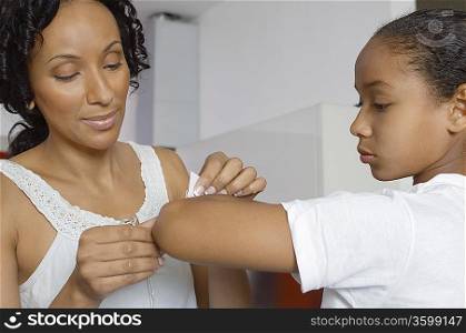 Mother applying bandaid to daughter (7-9) indoors