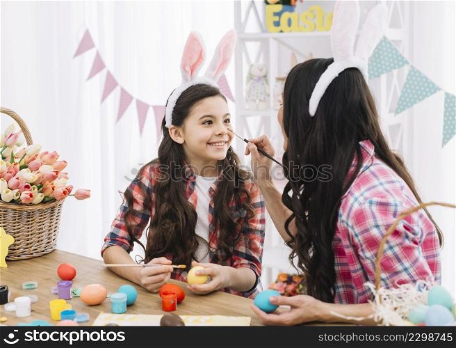mother applying color her daughter s nose while decorating easter eggs