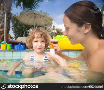 Mother applying sunblock lotion on child in swimming pool. Summer vacations concept