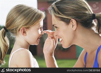 Mother applying sunscreen on daughter&acute;s (5-6) nose, smiling, side view, profile