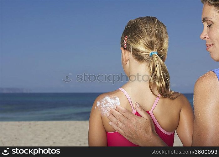 Mother applying sunscreen to daughter&acute;s (5-6) back, back view