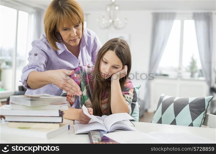 Mother assisting bored girl in studying at home