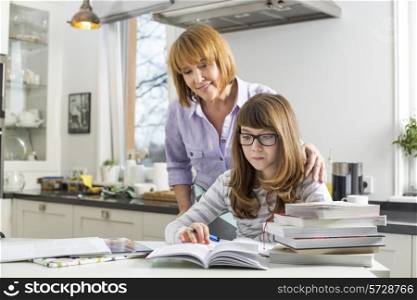Mother assisting daughter in doing homework in kitchen