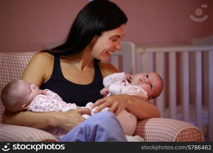 Mother At Home Cuddling Twin Baby Daughters In Nursery