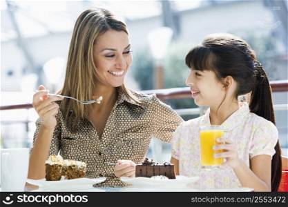 Mother at restaurant with daughter eating dessert and smiling (selective focus)