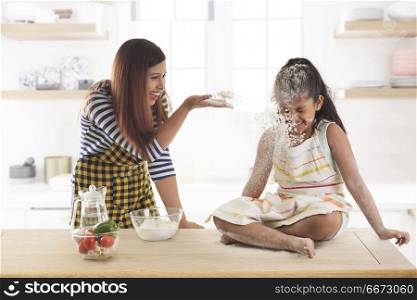 Mother blowing flour over daughter in kitchen