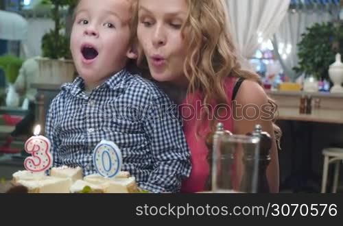 Mother blowing out the candles, her little son helping her. They succeds in it and mother claps her hands