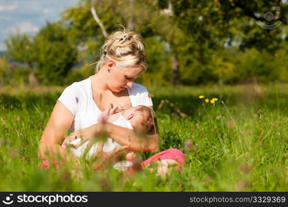 Mother breastfeeding her baby on a great sunny day in a meadow with lots of green grass and wild flowers